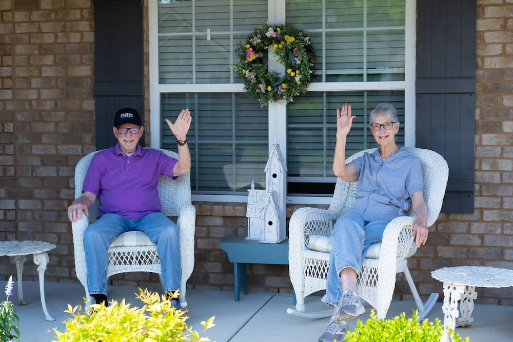 Elderly couple sitting on the front porch waving