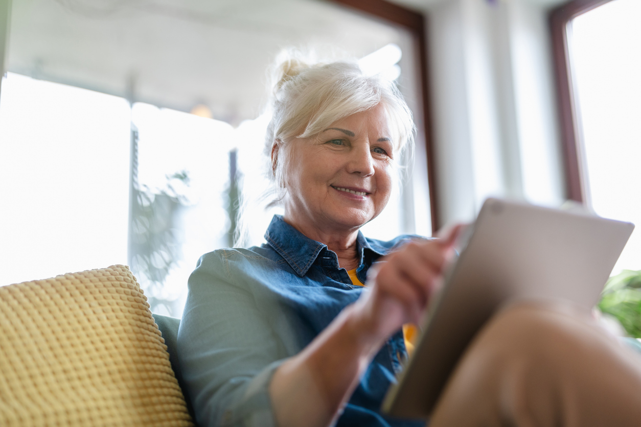 Mature woman using digital tablet while sitting on sofa at home.