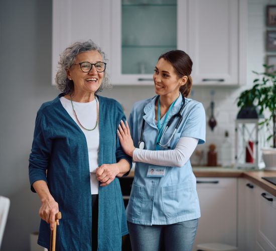 Nurse walking senior adult woman through the kitchen.