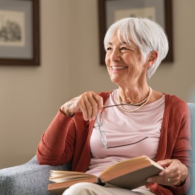 Senior adult smiling while reading book.