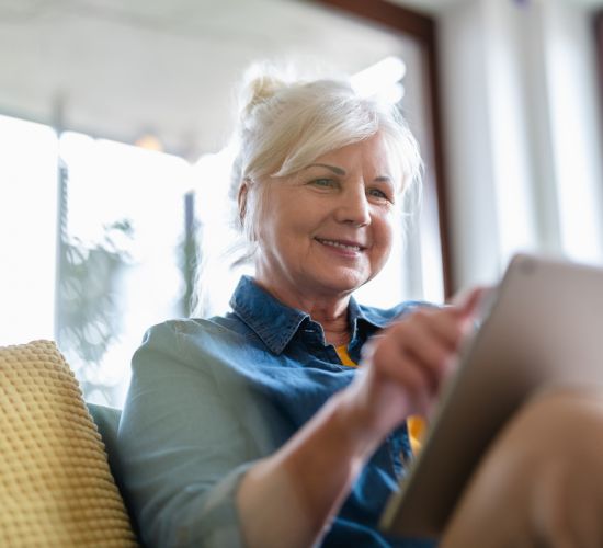 Mature woman using digital tablet while sitting on sofa at home.