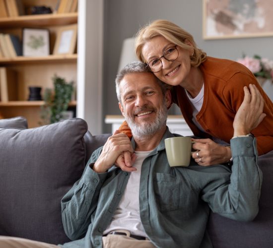 Mature couple smiling while sitting on couch.